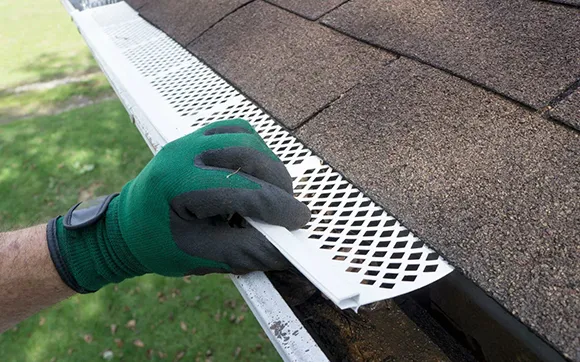 Hand installing metal gutter guard on residential roof for heavy rain protection in Quincy, MA