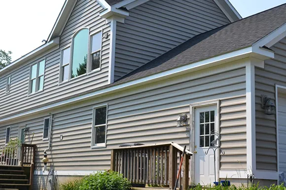 Gray vinyl siding on a large colonial style home in Quincy, MA with windows and railing visible.